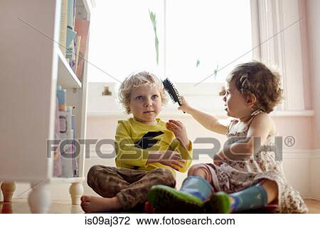 Stock Image - Female toddler brushing male toddlers hair in playroom. Fotosearch