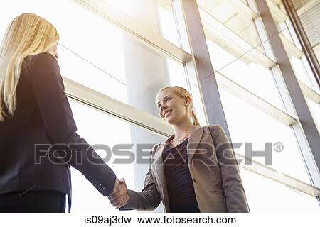 Low angle view of two young businesswomen shaking hands in office View Large Photo Image Stock Photo - Low angle view of two young businesswomen shaking hands in office. Fotosearch