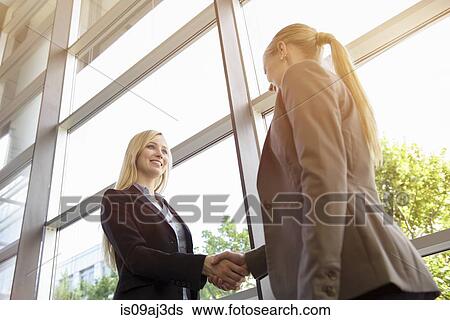Stock Photograph - Low angle view of two young businesswomen shaking hands. Fotosearch