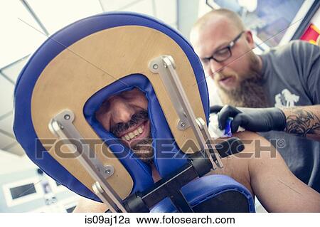 Stock Image - Male customers face between headrest in tattoo parlor. Fotosearch