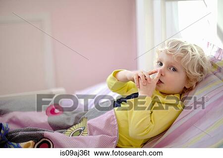 Stock Photograph - Male toddler lying in bed making secret hand gesture sign. Fotosearch