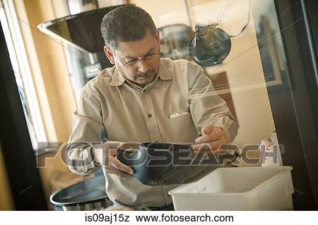 Stock Photo - Mature man using coffee bean scoop for coffee roasting machine in cafe. Fotosearch