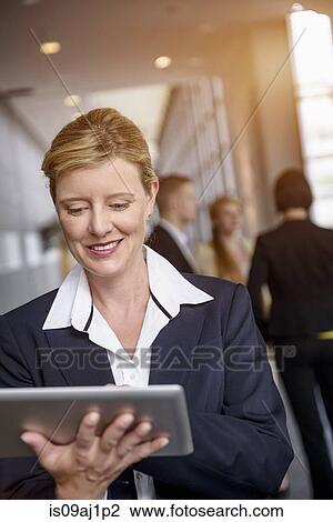 Mature woman using touchscreen on digital tablet in office corridor View Large Photo Image Stock Image - Mature woman using touchscreen on digital tablet in office corridor. Fotosearch