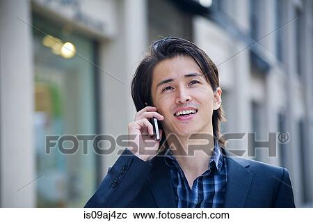 Stock Image - Mid adult businessman chatting on smartphone on city street. Fotosearch