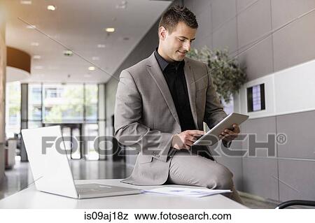 Mid adult businessman on office desk using digital tablet View Large Photo Image Stock Photo - Mid adult businessman on office desk using digital tablet. Fotosearch
