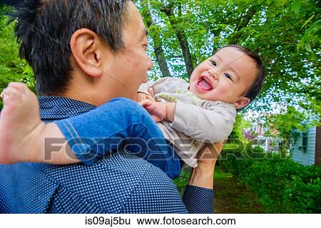 Mid adult father playing with baby son in garden View Large Photo Image Stock Photograph - Mid adult father playing with baby son in garden. Fotosearch