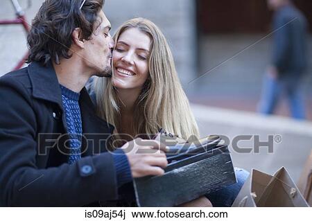 Stock Image - Mid adult man receiving gift of shoes from girlfriend on city street. Fotosearch