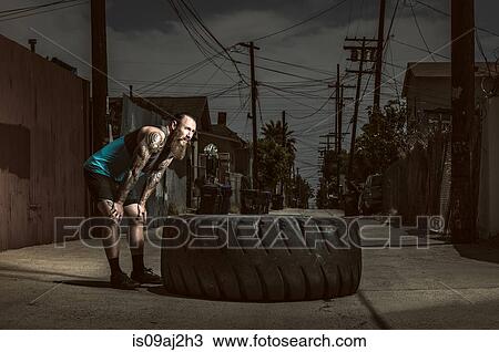 Stock Image - Mid adult man standing by large tire. Fotosearch