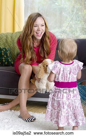 Stock Image - Mid adult mother playing with baby daughter and soft toy dog. Fotosearch