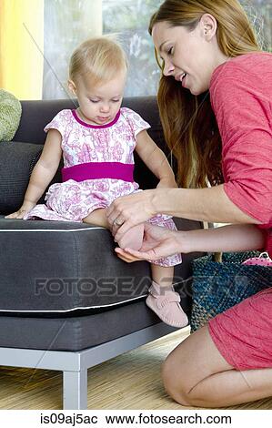Stock Image - Mid adult mother putting on baby daughter's shoes. Fotosearch