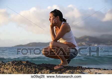 Stock Photograph - Mid adult woman crouching and gazing at caribbean sea from pier, Spice Island beach resort, Grenada,. Fotosearch