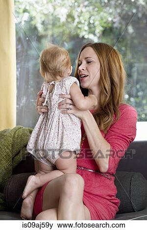 Mid adult woman holding up baby daughter on sofa View Large Photo Image Stock Photo - Mid adult woman holding up baby daughter on sofa. Fotosearch