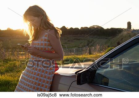 Mid adult woman leaning against car texting on smartphone View Large Photo Image Stock Photo - Mid adult woman leaning against car texting on smartphone. Fotosearch