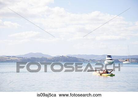 Stock Image - Mid adult woman lying on her back paddleboarding at sea. Fotosearch