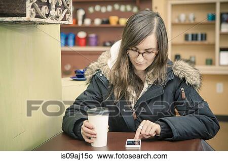 Mid adult woman texting on smartphone in cafe View Large Photo Image Picture - Mid adult woman texting on smartphone in cafe. Fotosearch