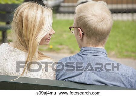 Over the shoulder view of young couple on park bench View Large Photo Image Stock Photograph - Over the shoulder view of young couple on park bench. Fotosearch