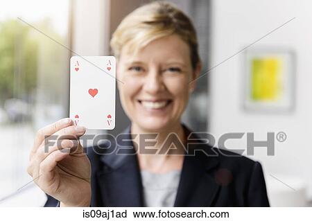 Stock Image - Portrait of mature businesswoman holding up ace playing card. Fotosearch
