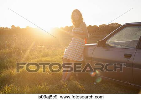 Stock Photo - Portrait of mid adult woman leaning against car at sunset. Fotosearch