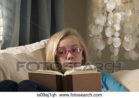 Stock Image - Portrait of pre adolescent girl staring over reading book. Fotosearch