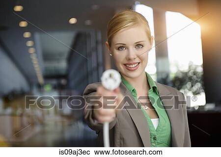 Stock Image - Portrait of smiling young businesswoman holding up network power cable in office. Fotosearch