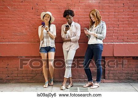 Stock Photograph - Portrait of three young women using mobile phones. Fotosearch
