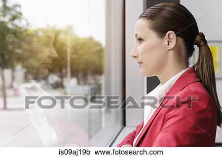 Stock Image - Portrait of unhappy young businesswoman gazing through window. Fotosearch