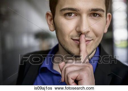 Portrait of young businessman with finger on lips in office View Large Photo Image Stock Photograph - Portrait of young businessman with finger on lips in office. Fotosearch