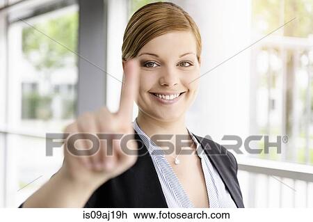 Stock Image - Portrait of young businesswoman holding up a finger. Fotosearch