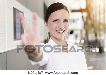 Stock Photo - Portrait of young businesswoman holding up hand in victory sign. Fotosearch