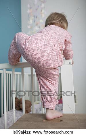 Stock Photo - Rear view of female toddler climbing over side of crib. Fotosearch
