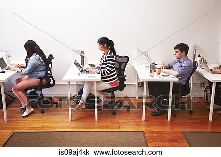 Row of people working at desks in office View Large Photo Image Stock Image - Row of people working at desks in office. Fotosearch