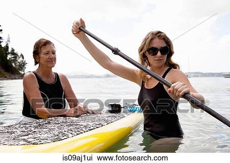 Senior woman and daughter wading with paddleboard at sea View Large Photo Image Stock Image - Senior woman and daughter wading with paddleboard at sea. Fotosearch