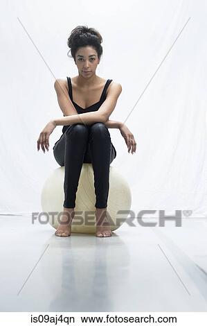 Picture - Studio portrait of confident young woman sitting on exercise ball. Fotosearch