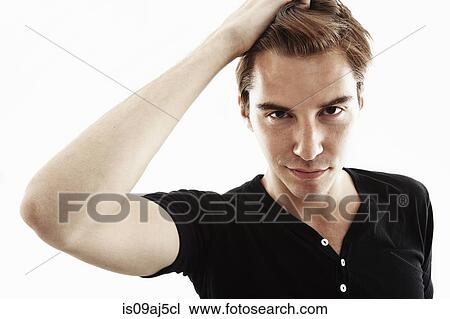 Stock Image - Studio portrait of young man with hand in hair. Fotosearch