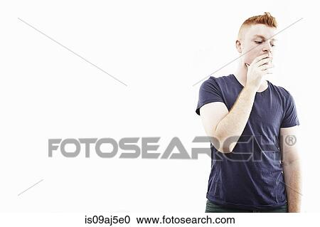 Stock Image - Studio portrait of young man with hand over mouth. Fotosearch