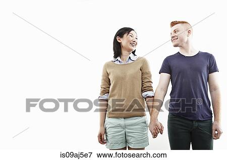 Stock Photo - Studio shot of smiling young couple holding hands. Fotosearch