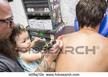 Stock Image - Tattoo artist showing toddler how to give a tattoo. Fotosearch