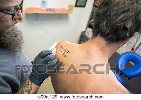 Tattooist marking out "my first tattoo" on customer's shoulder View Large Photo Image Stock Photo - Tattooist marking out "my first tattoo" on customer's shoulder. Fotosearch