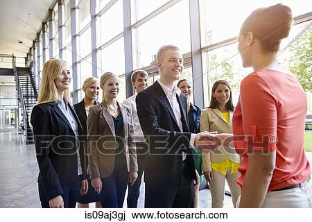 Stock Image - Team of business men and women greeting client in office. Fotosearch