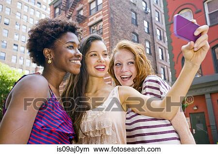 Three young women taking picture of themselves using mobile phone View Large Photo Image Picture - Three young women taking picture of themselves using mobile phone. Fotosearch