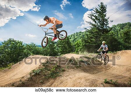 Stock Image - Two male friends riding BMX and mountain bikes on rural pump track. Fotosearch