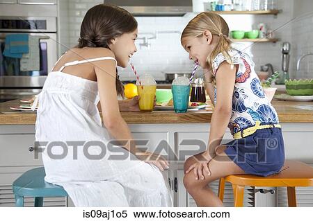 Two mischievous sisters blowing bubbles through straws at breakfast bar View Large Photo Image Stock Photography - Two mischievous sisters blowing bubbles through straws at breakfast bar. Fotosearch