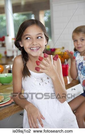 Stock Image - Two mischievous sisters with raspberries on their fingers in kitchen. Fotosearch