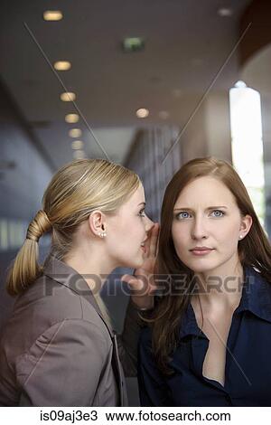 Stock Image - Two serious young businesswomen whispering in office. Fotosearch