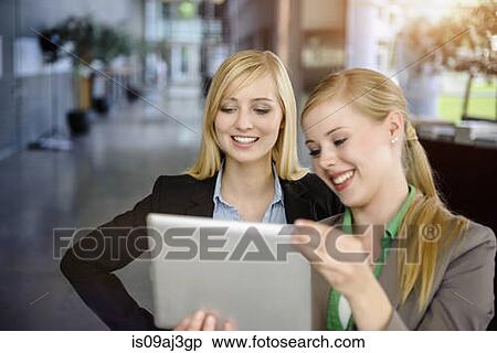 Stock Photography - Two young businesswomen looking at digital tablet in office. Fotosearch