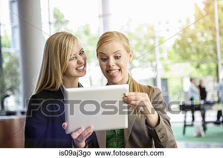 Picture - Two young businesswomen pulling faces and taking self portrait on digital tablet in office. Fotosearch