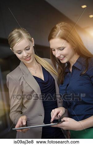 Two young businesswomen using touchscreen on digital tablet in office View Large Photo Image Stock Photo - Two young businesswomen using touchscreen on digital tablet in office. Fotosearch