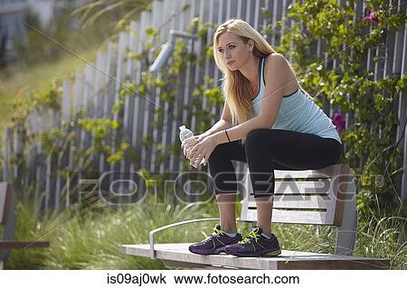 Stock Image - Woman sitting on top of park bench. Fotosearch