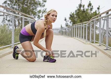 Stock Image - Woman tying shoe lace on bridge. Fotosearch