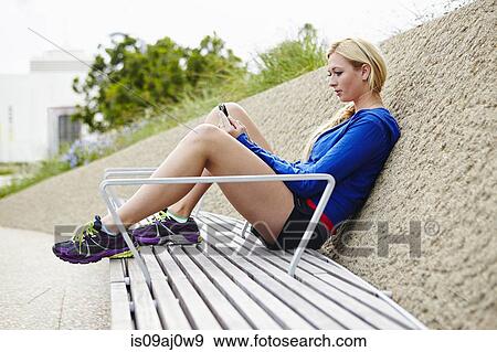 Stock Photo - Woman using smartphone on park bench. Fotosearch